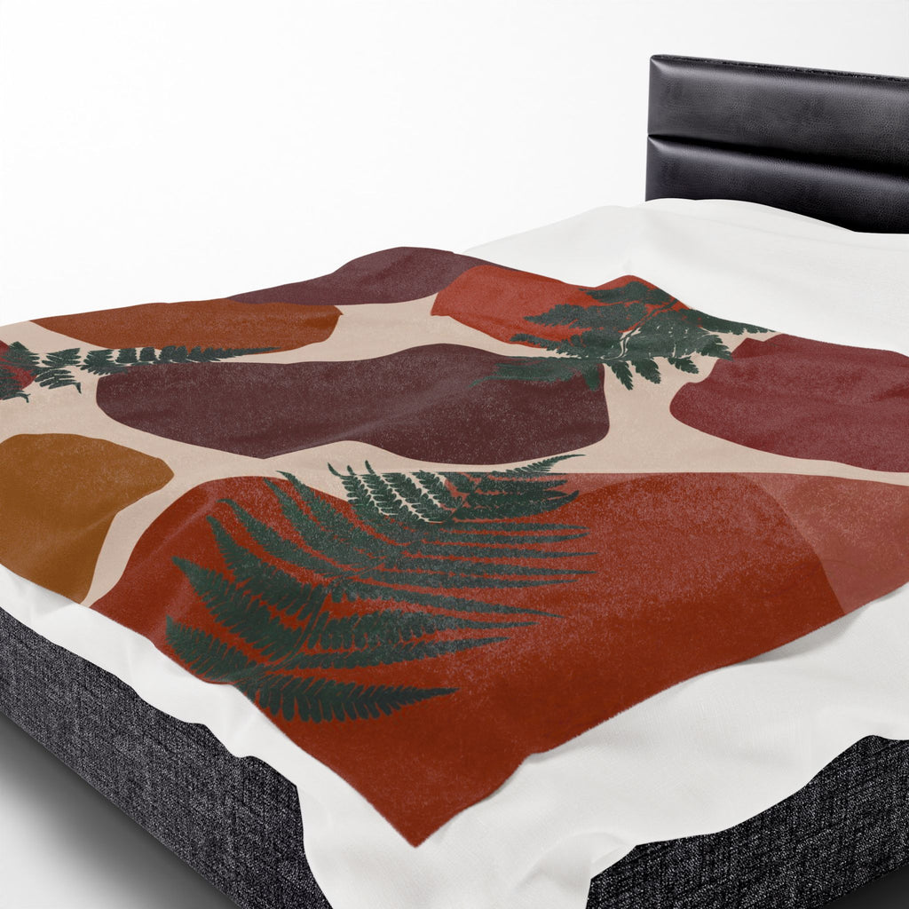 Bed with a fern pattern throw blanket featuring red, brown, and green colors on a white background.