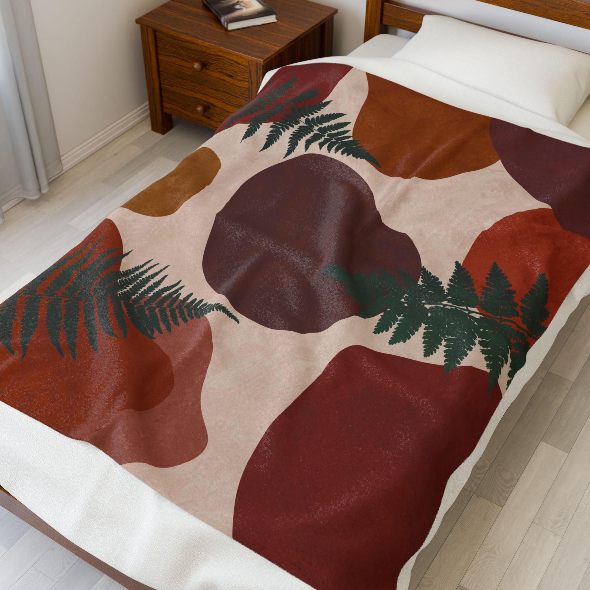 Bed with fern patterned blanket with warm geometric shapes in rust, dark red, burgundy and orange on beige in a bedroom setting