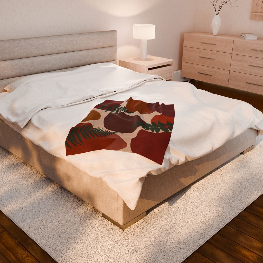 Bedroom with a bed featuring a decorative throw blanket and wooden furniture. The velveteen blanket features ferns and abstract geometric shapes.