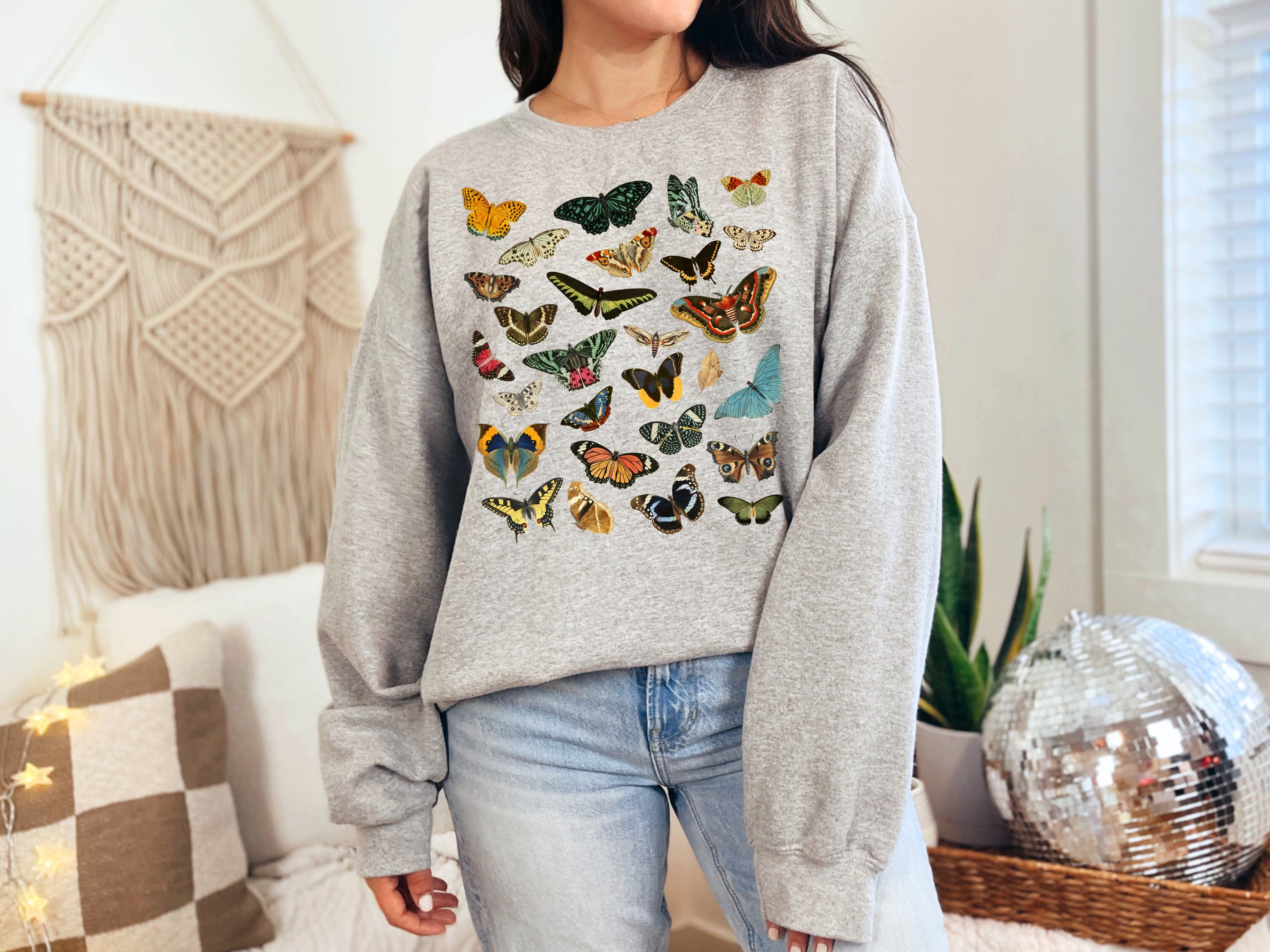 Person wearing a gray sweatshirt with colorful butterfly & moth patterns in a cozy room.