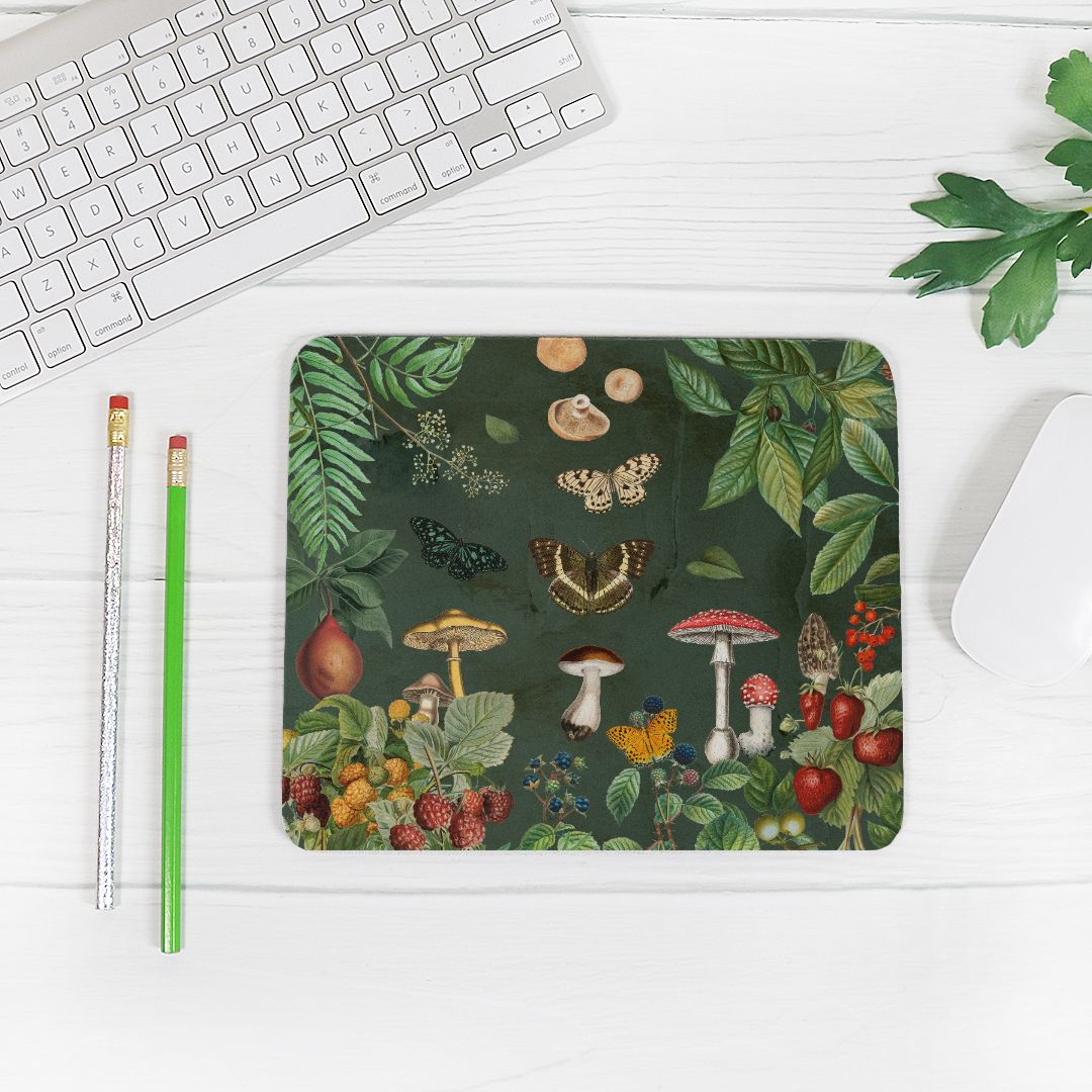 Nature inspired desk décor mouse pad on a white wooden surface next to a keyboard and mouse. Butterfies, Berries and Mushrooms on a dark green backgroud