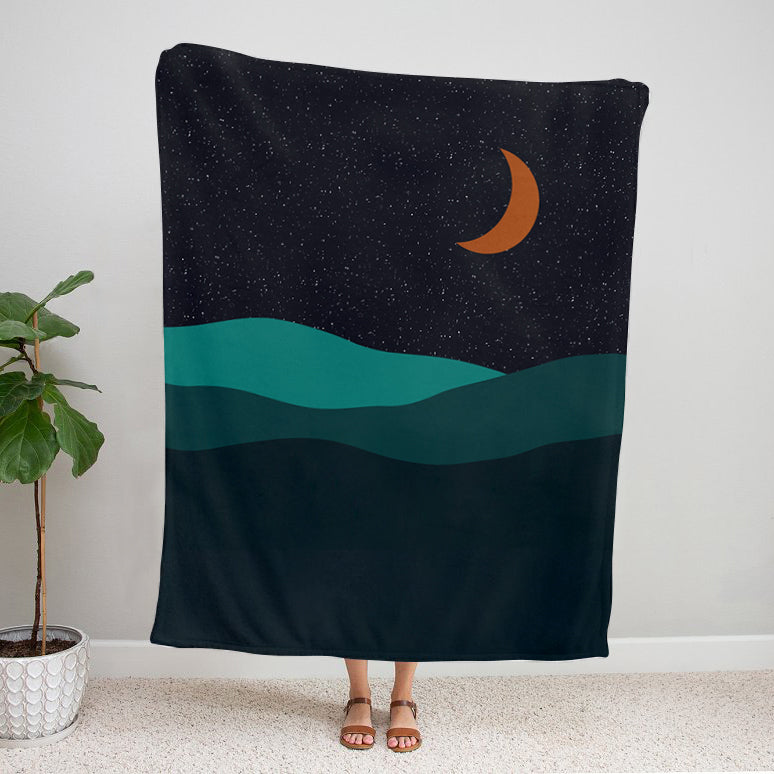 Velveteen plush blanket with a desert moon design, starry night sky, and teal layered hills
