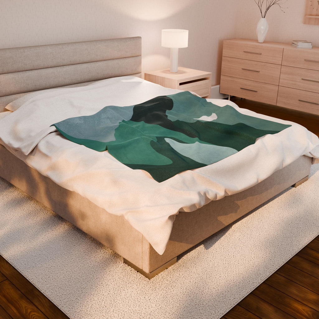 Bed with a green and teal abstract mountain design blanket in a bedroom setting. 50x60 inch velveteen blanket