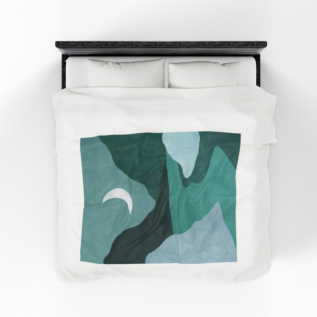 Bed with white bedding and a green abstract mountain & moon patterned throw blanket. 50x60 inch velveteen plush blanket.