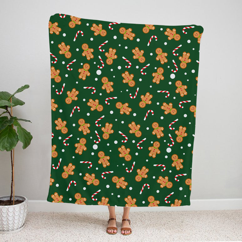 Green blanket with gingerbread man and candy cane pattern draped over a person, with a plant in the corner.