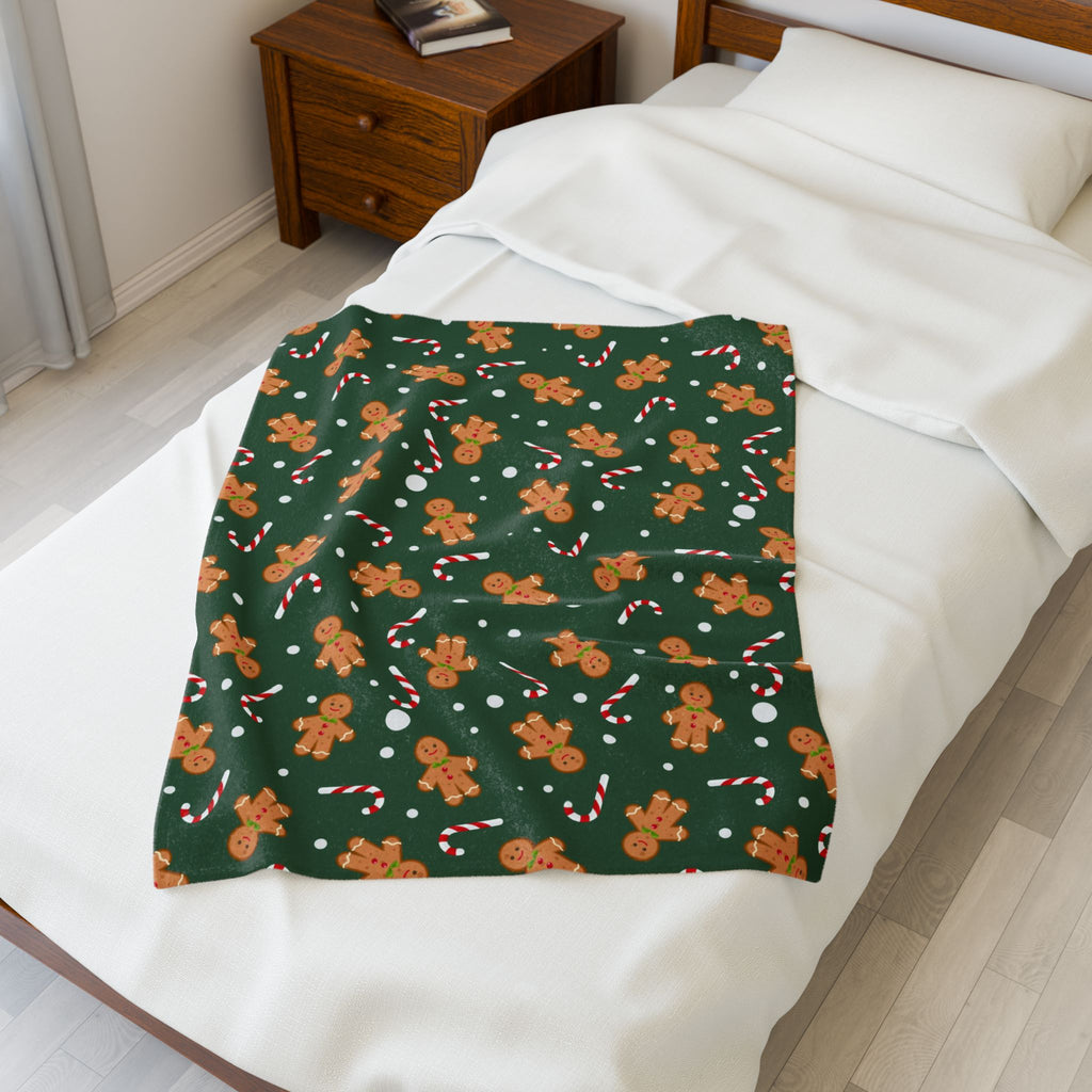 Green blanket with gingerbread man & candy cane pattern draped over a bed.