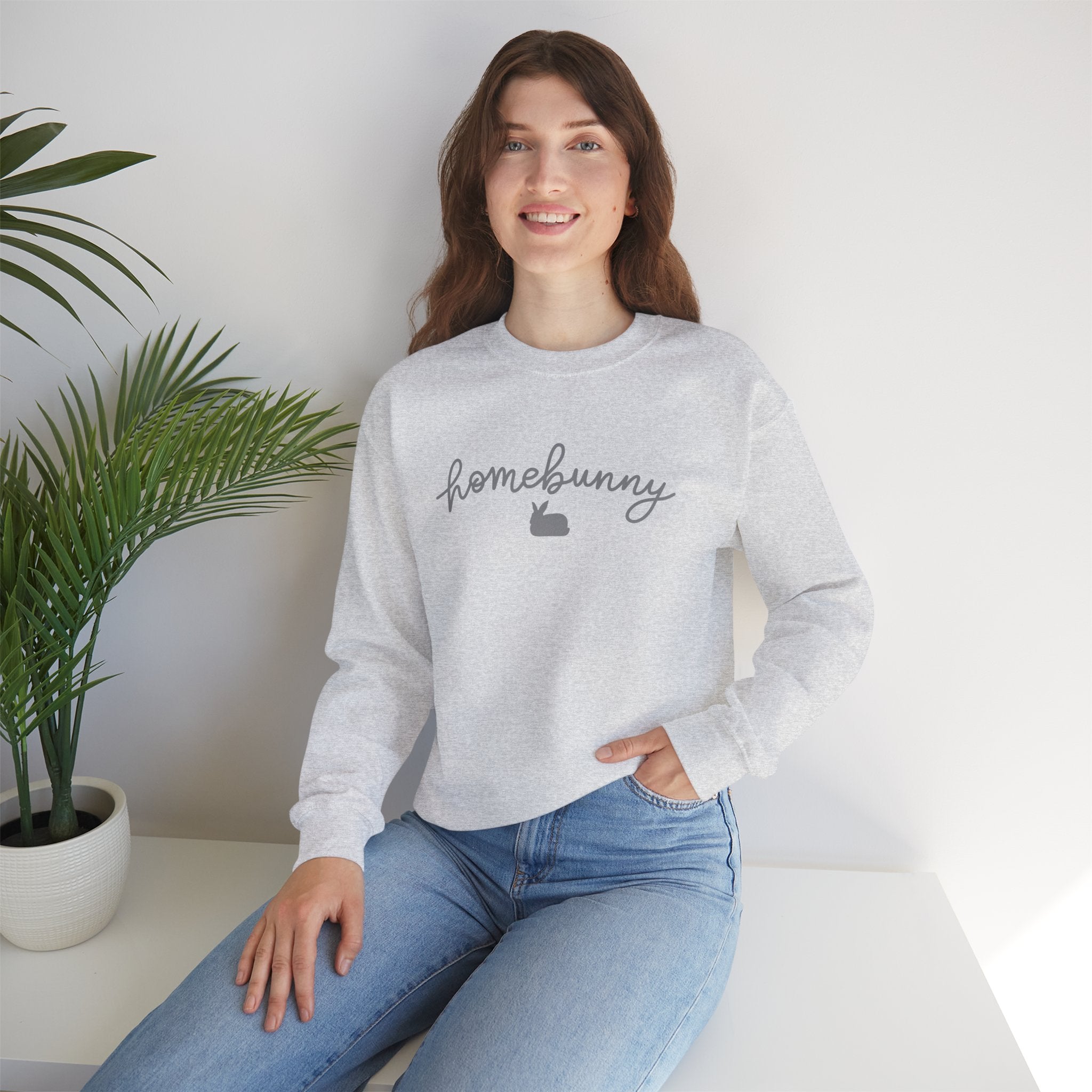 Woman wearing a ash gray sweatshirt with 'homebunny' text, sitting in a room with a plant.