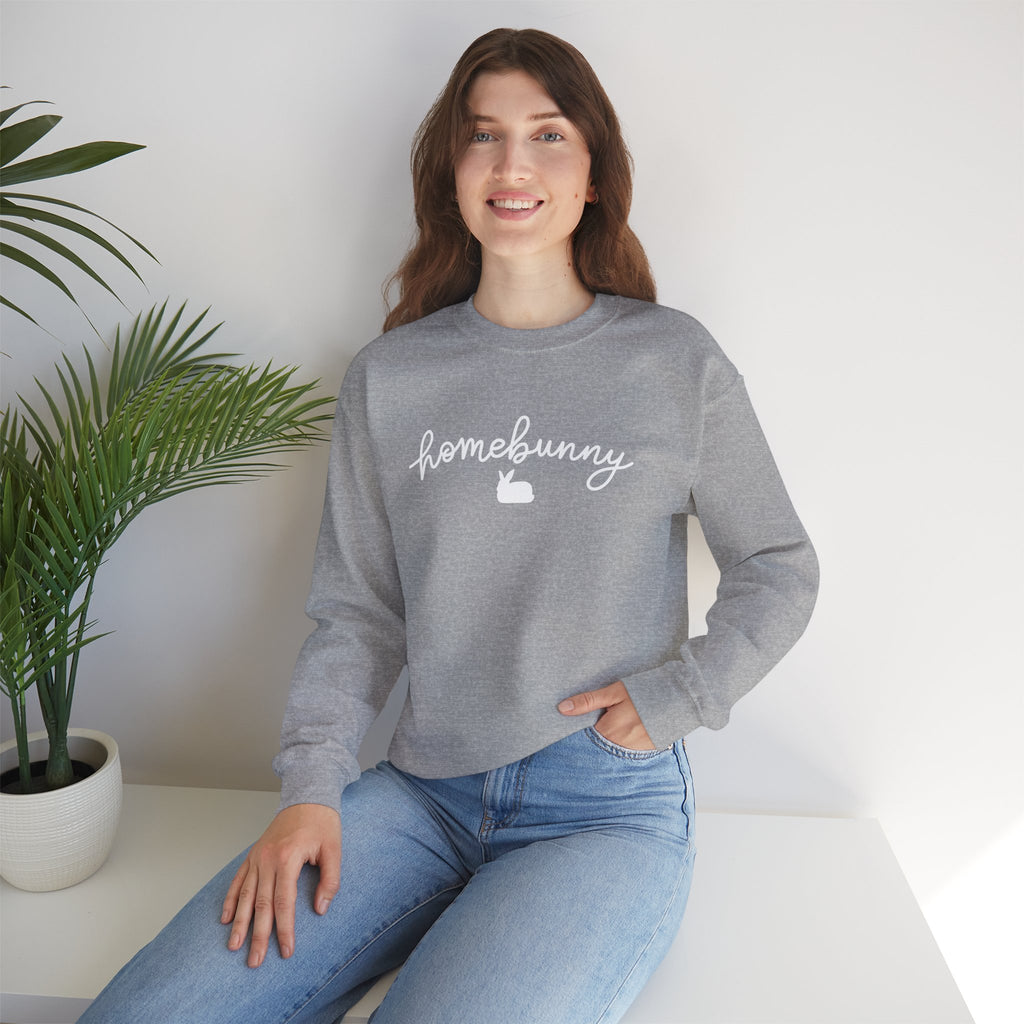 Woman wearing a sport gray sweatshirt with 'homebunny' text, sitting in a room with a plant.
