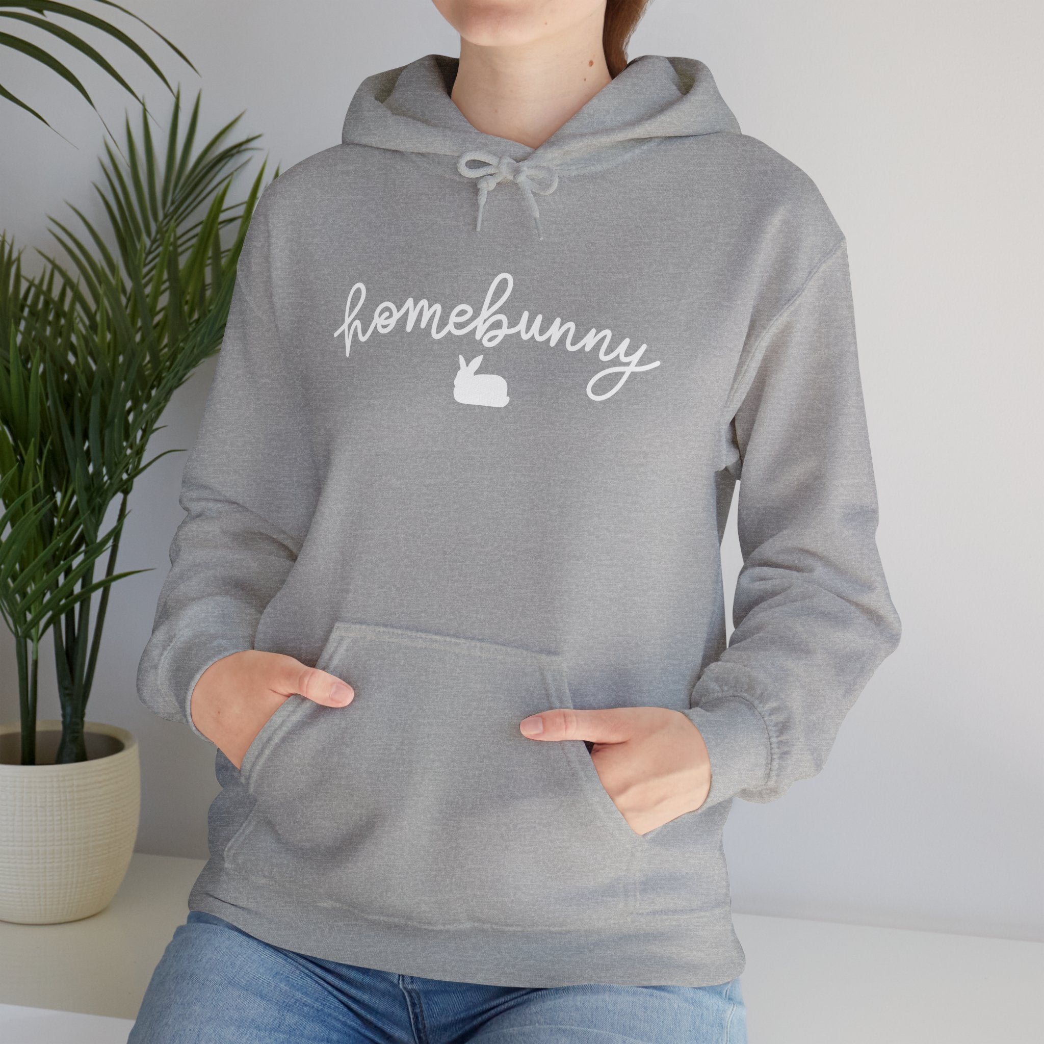 Person wearing a Gildan sport gray hoodie with 'homebunny' text, standing indoors with a plant in the background.