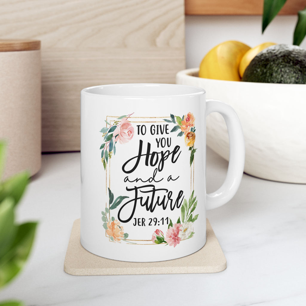 White mug with floral design and text on a coaster, placed on a surface with plants and fruit in the background. Bible Verse Jeremiah 29:11