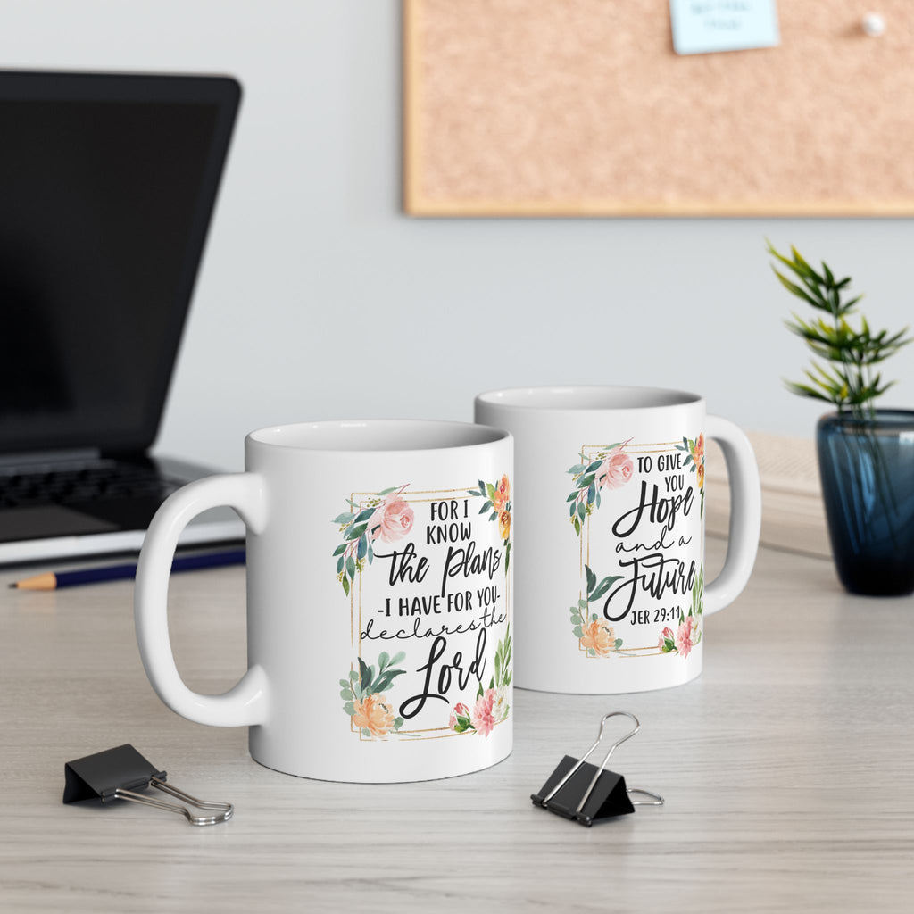 Two mugs with Christian motivational quotes on a desk with a laptop and plant in the background