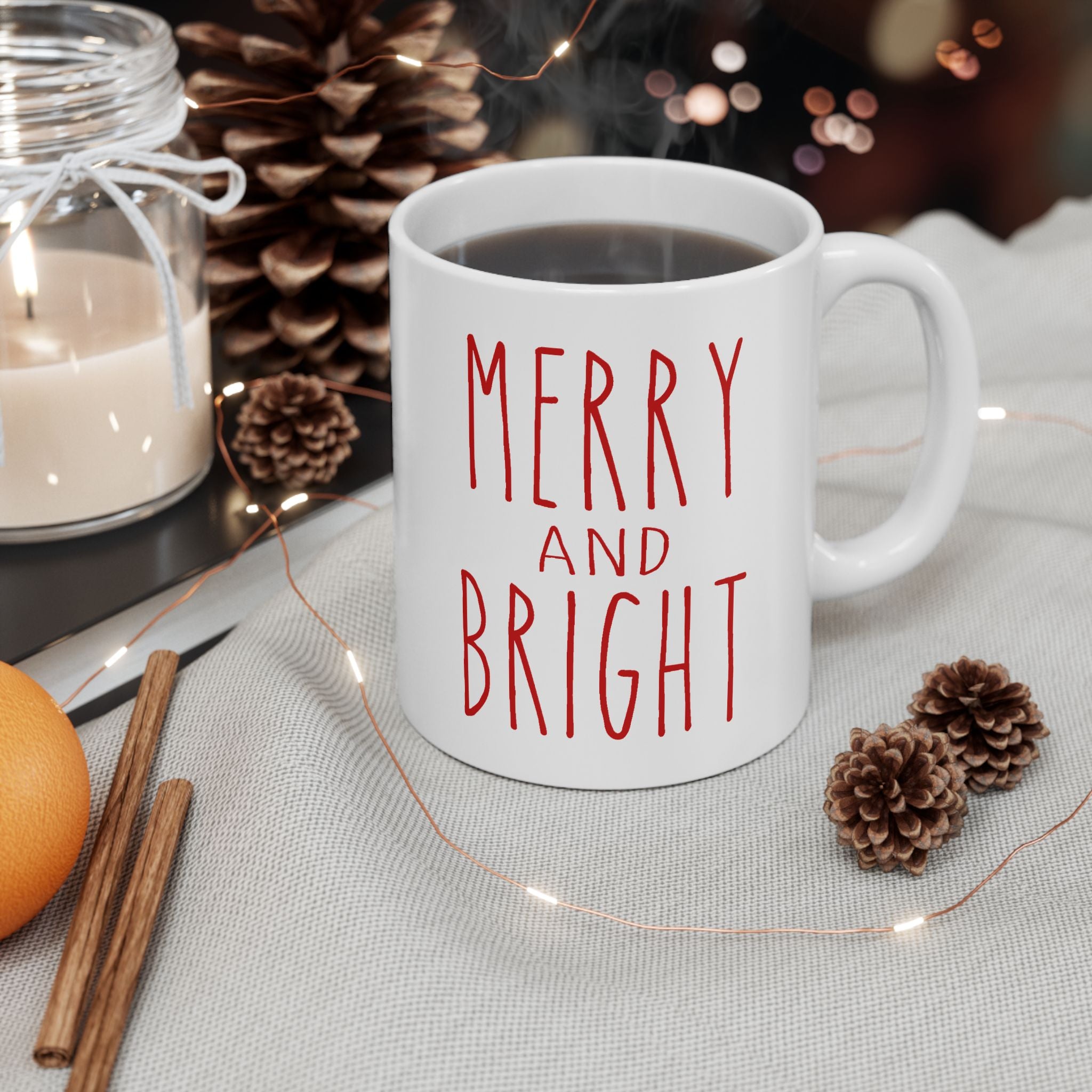 White mug with 'Merry and Bright' text on a table with Christmas decorations.