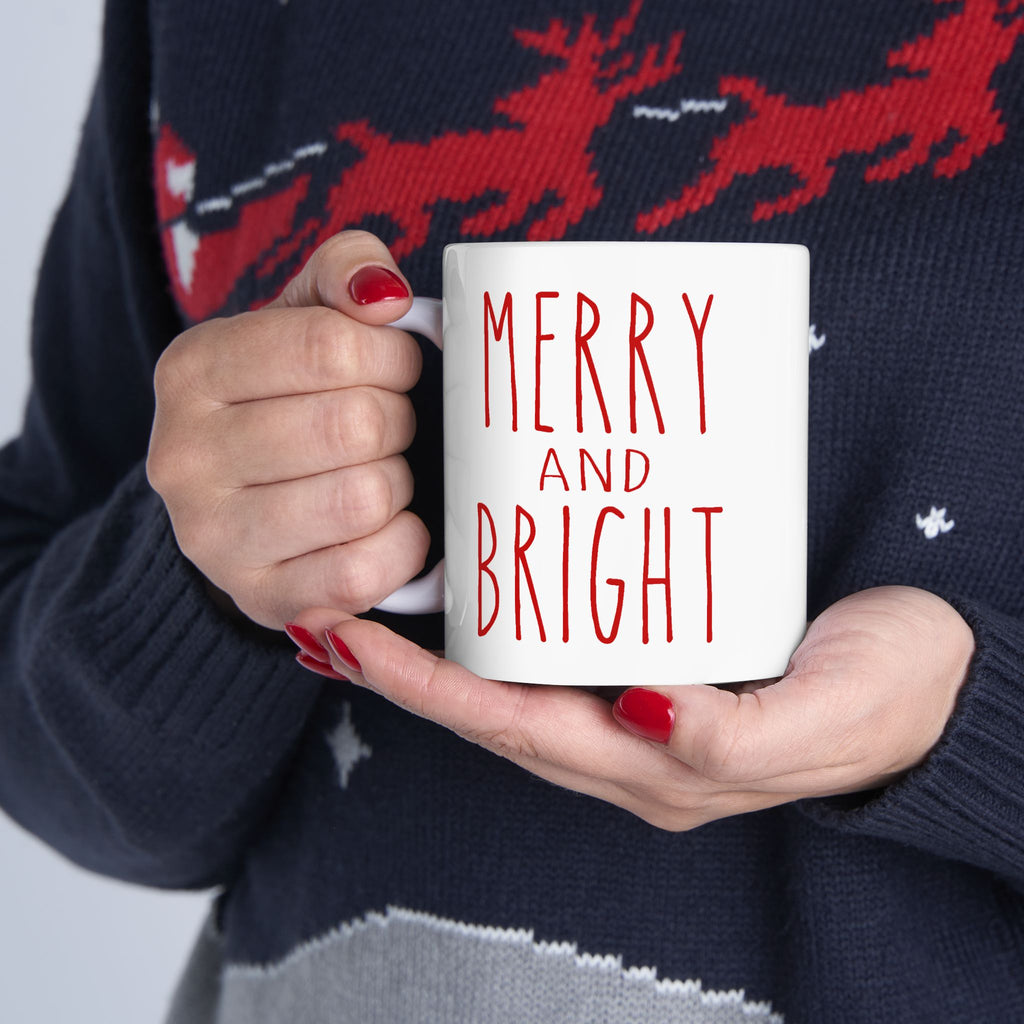 Person holding a mug with 'Merry and Bright' text, wearing a festive sweater.