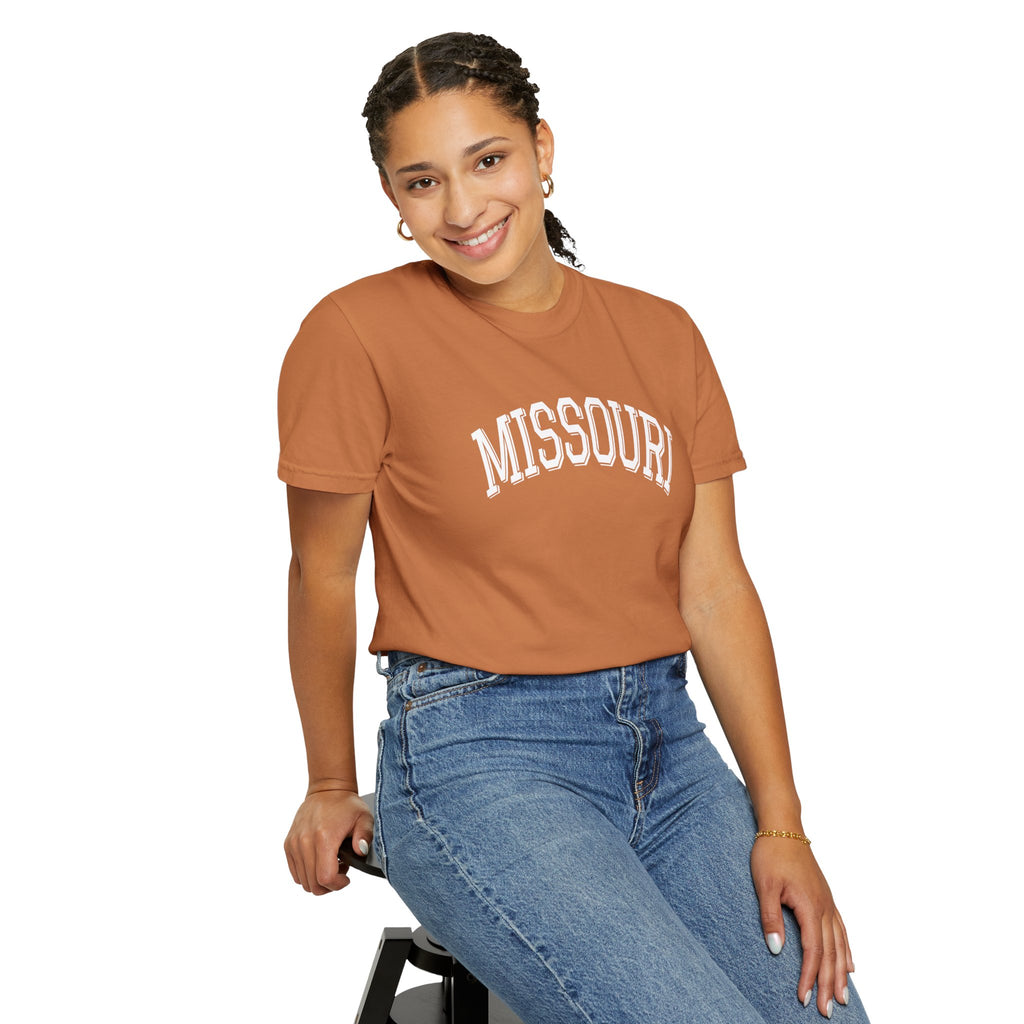 Person wearing a muted orange 'Missouri' Comfort Colors t-shirt in color Yam and blue jeans on a white background