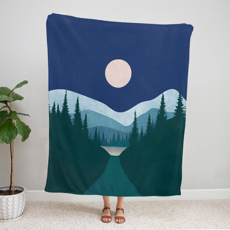 Blanket with a mountain and moon design draped over a person, with a plant on the side.