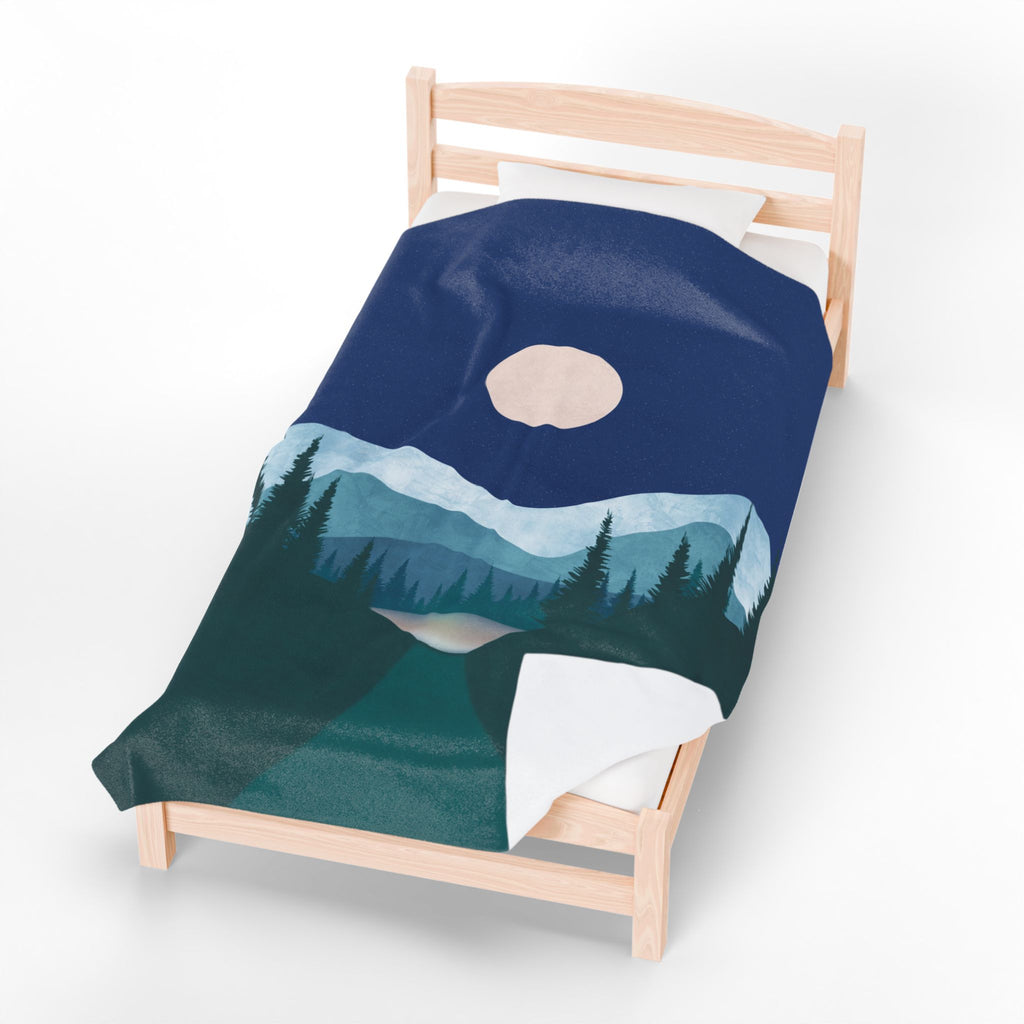 Blanket with mountain design draped over a wooden bed on a white background