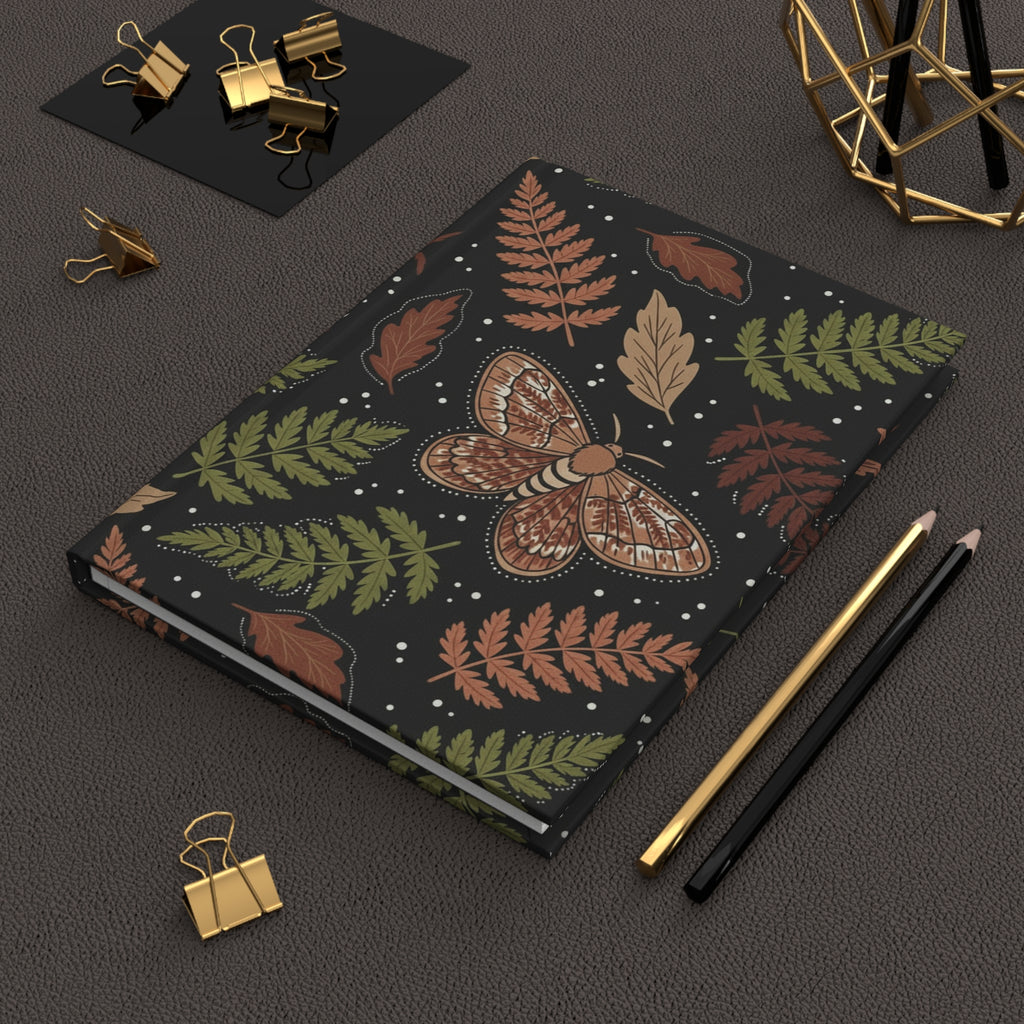 Notebook with moth and leaf design on a dark surface with stationery items.