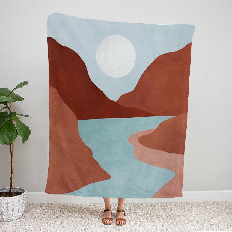 Abstract landscape Mountain stream velveteen plush blanket with canyon landscape, flowing river, and sun over hills, held by a person in a room.