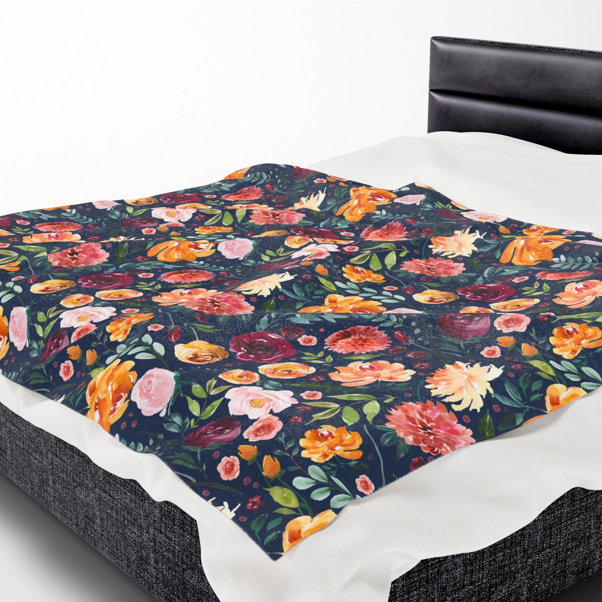 Floral patterned throw blanket on a bed with a white sheet and black headboard. Watercolor floral print.