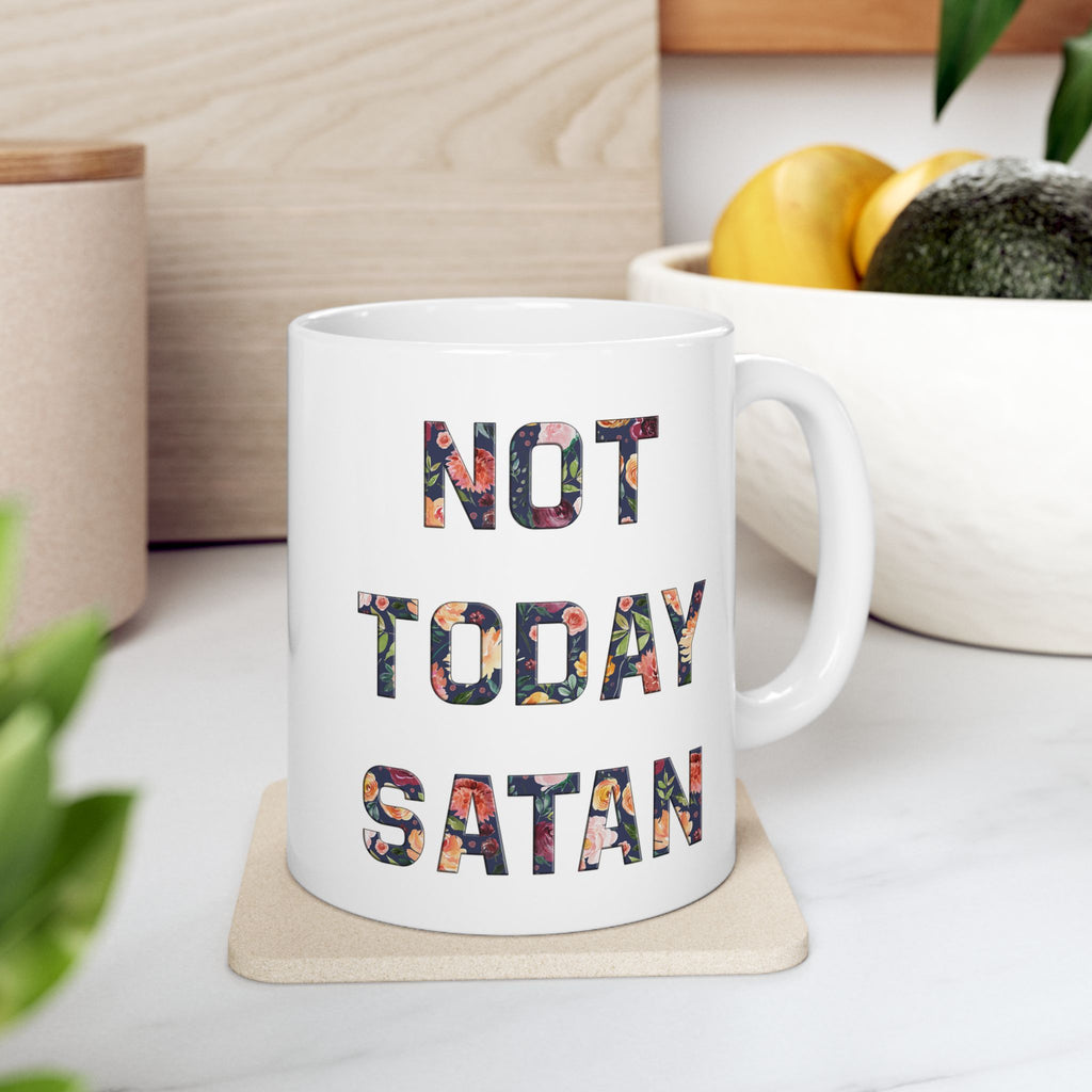 White mug with 'Not Today Satan' text on a wooden coaster, surrounded by plants and a bowl of fruit.