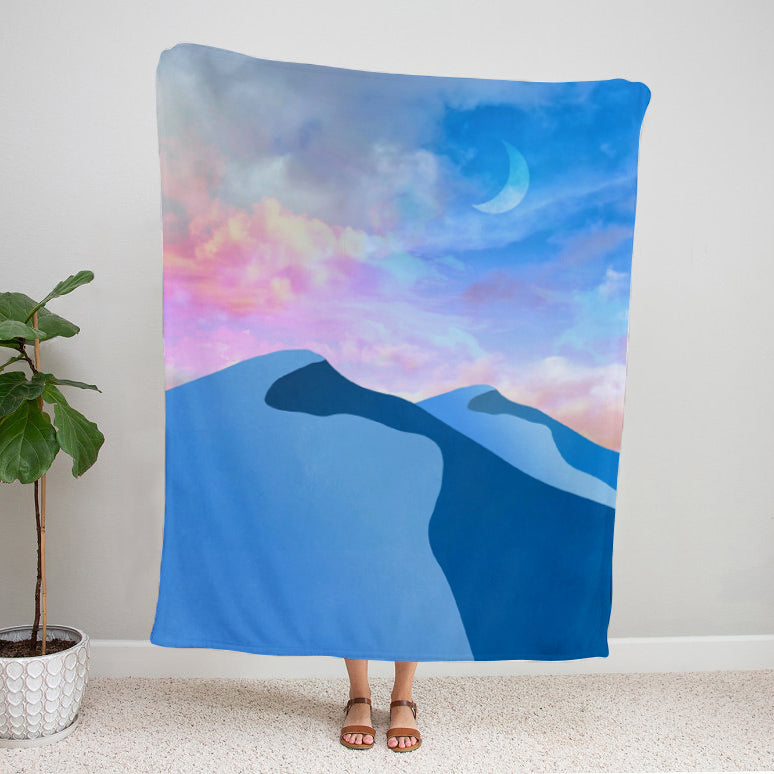 Colorful landscape blanket with mountains and a crescent moon with a person  holding blanket against a white wall.