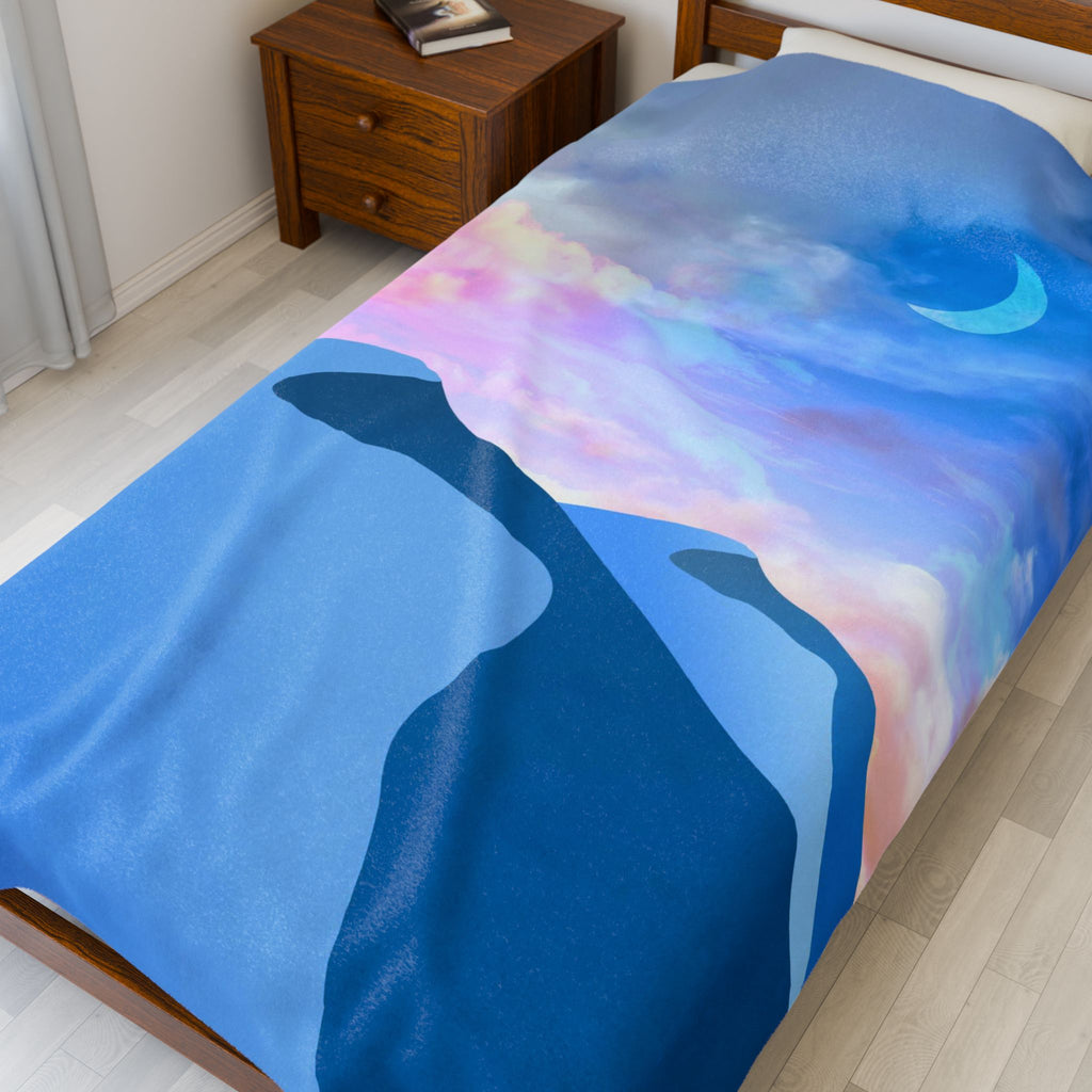 Bed with a colorful blanket featuring Desert mountains and a crescent moon.