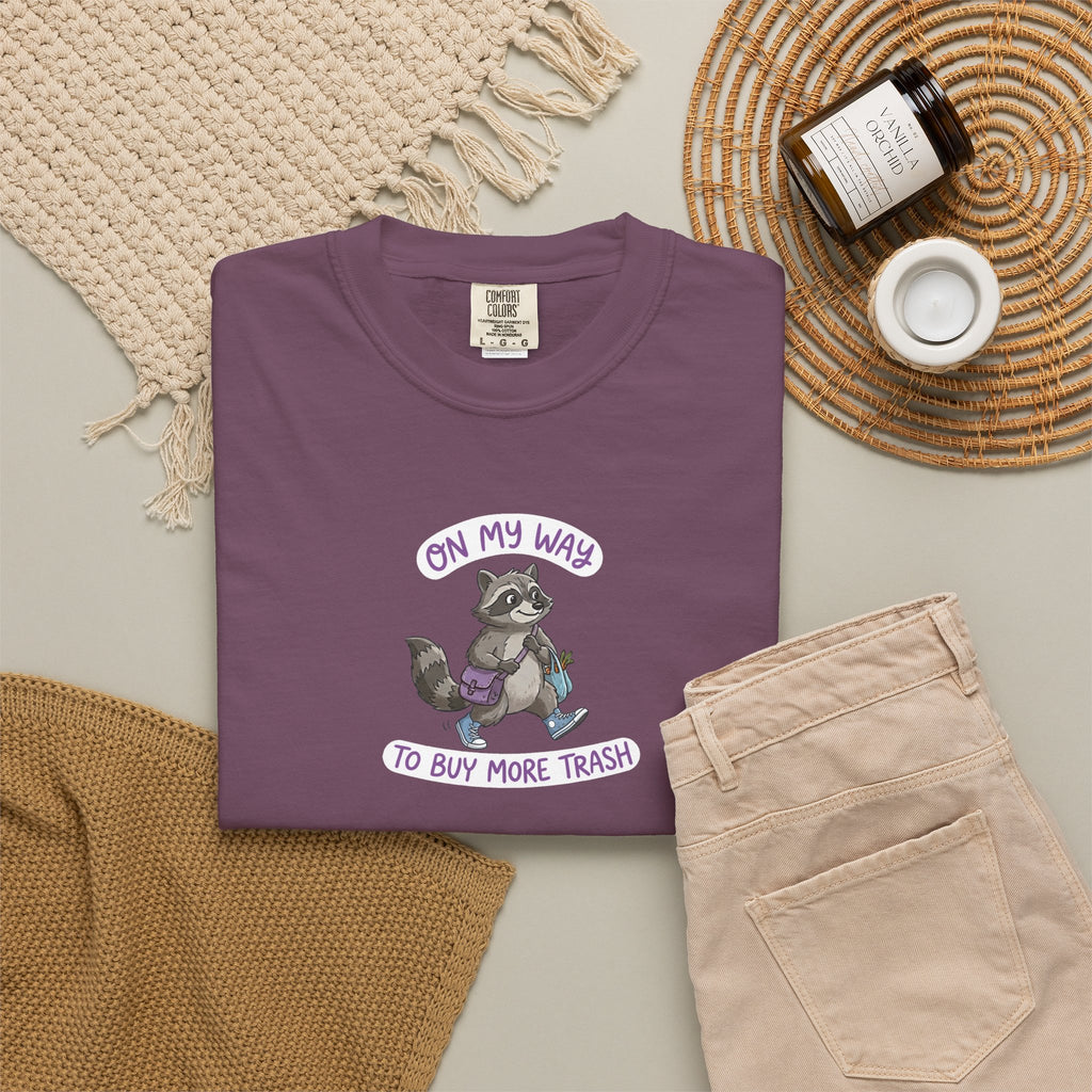 Berry t-shirt with a raccoon graphic and text on a neutral surface with accessories.