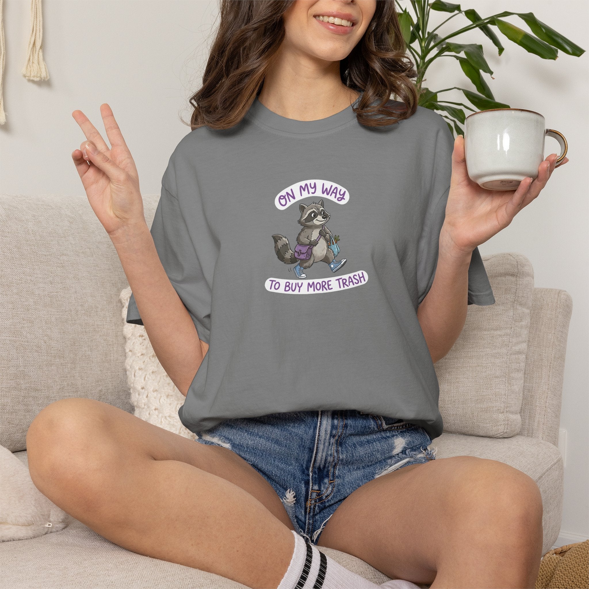 Person wearing a grey t-shirt with a graphic and text, holding a mug in a casual setting.