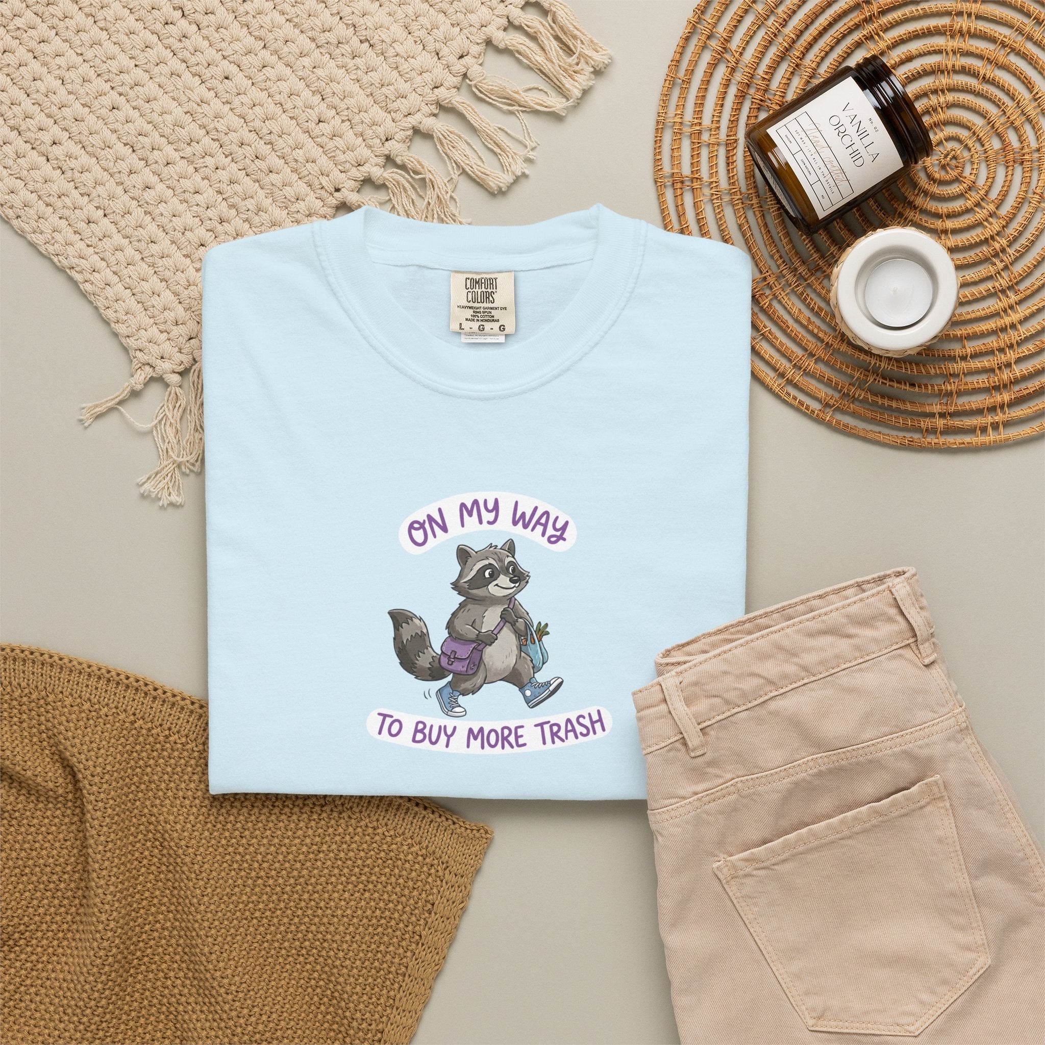 Light blue t-shirt with raccoon graphic and text on a neutral surface with accessories.