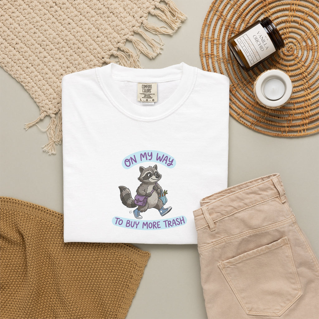 White t-shirt with raccoon graphic and text on a neutral surface with accessories.