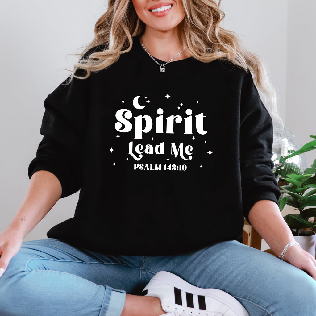 Woman wearing a black sweatshirt with 'Spirit Lead Me Psalm 143:10' text, sitting on the floor with plants in the background.