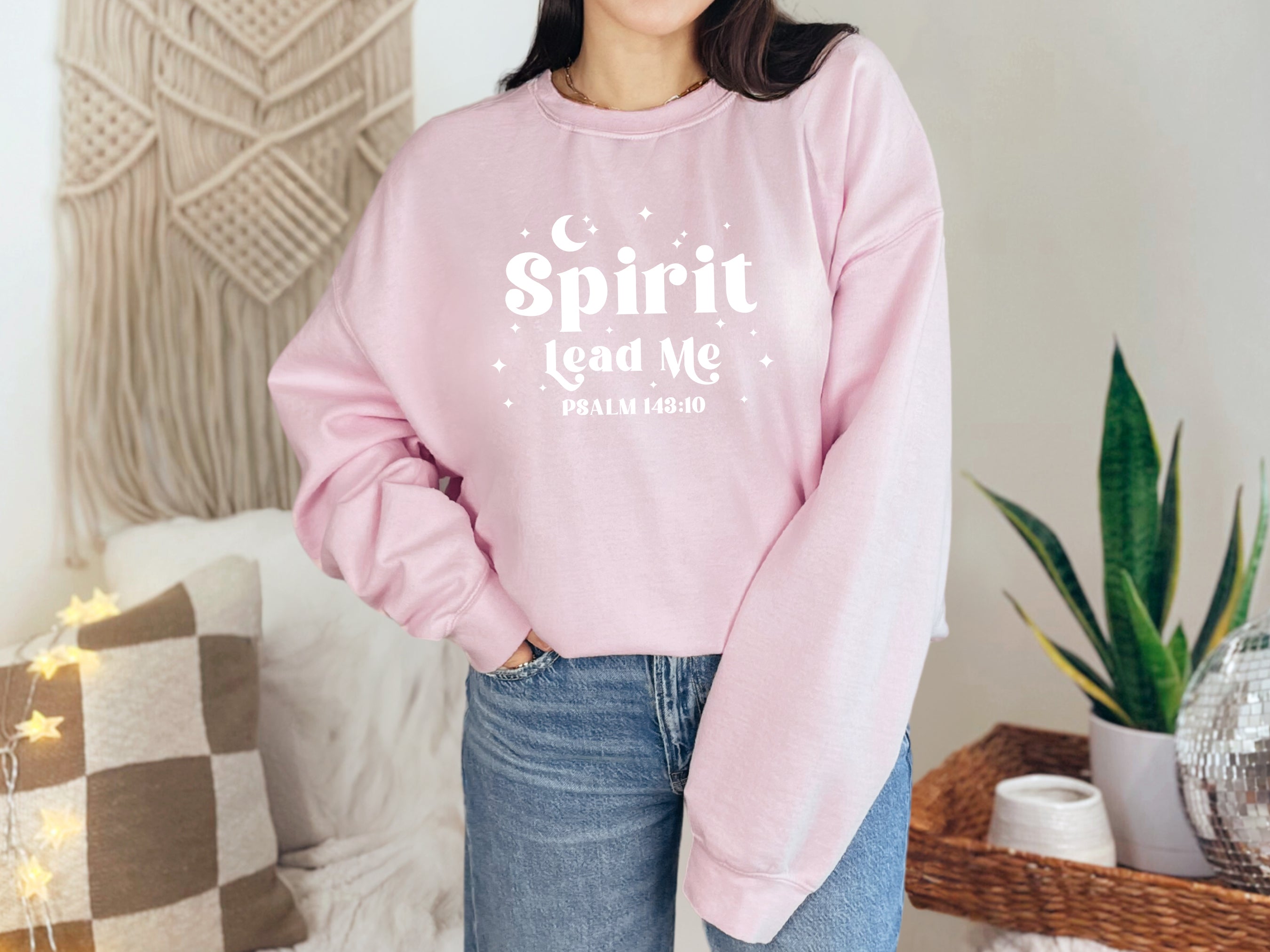 Person wearing a pink sweatshirt with 'Spirit Lead Me' text in a home setting. Bible Verse sweatshirt, Psalm 143:10