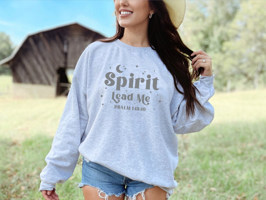 Woman wearing a gray sweatshirt with 'Spirit Lead Me' text in a field with a barn in the background