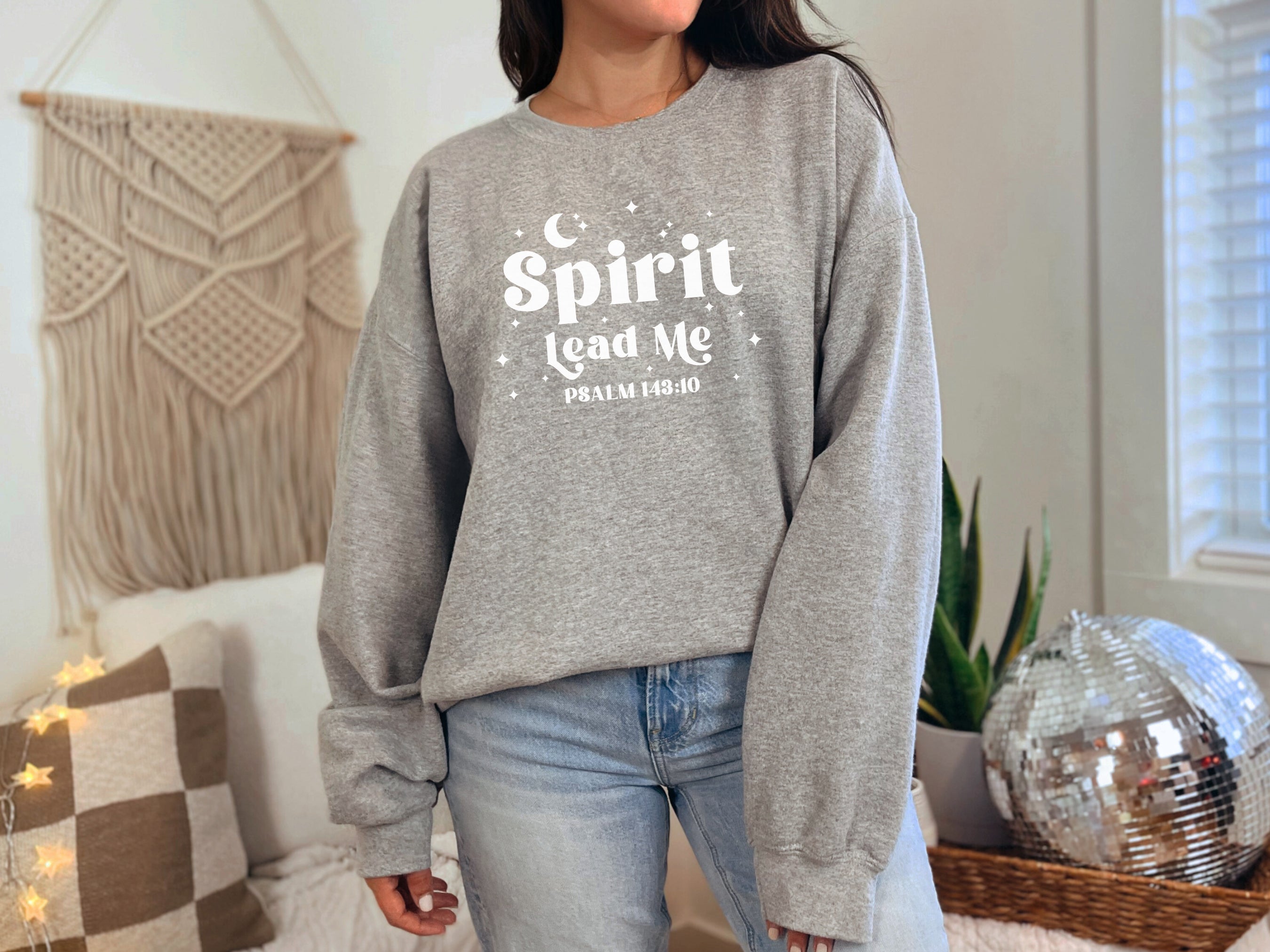 Person wearing a Gildan Sport gray sweatshirt with 'Spirit Lead Me' text in a home setting, bible verse sweatshirt