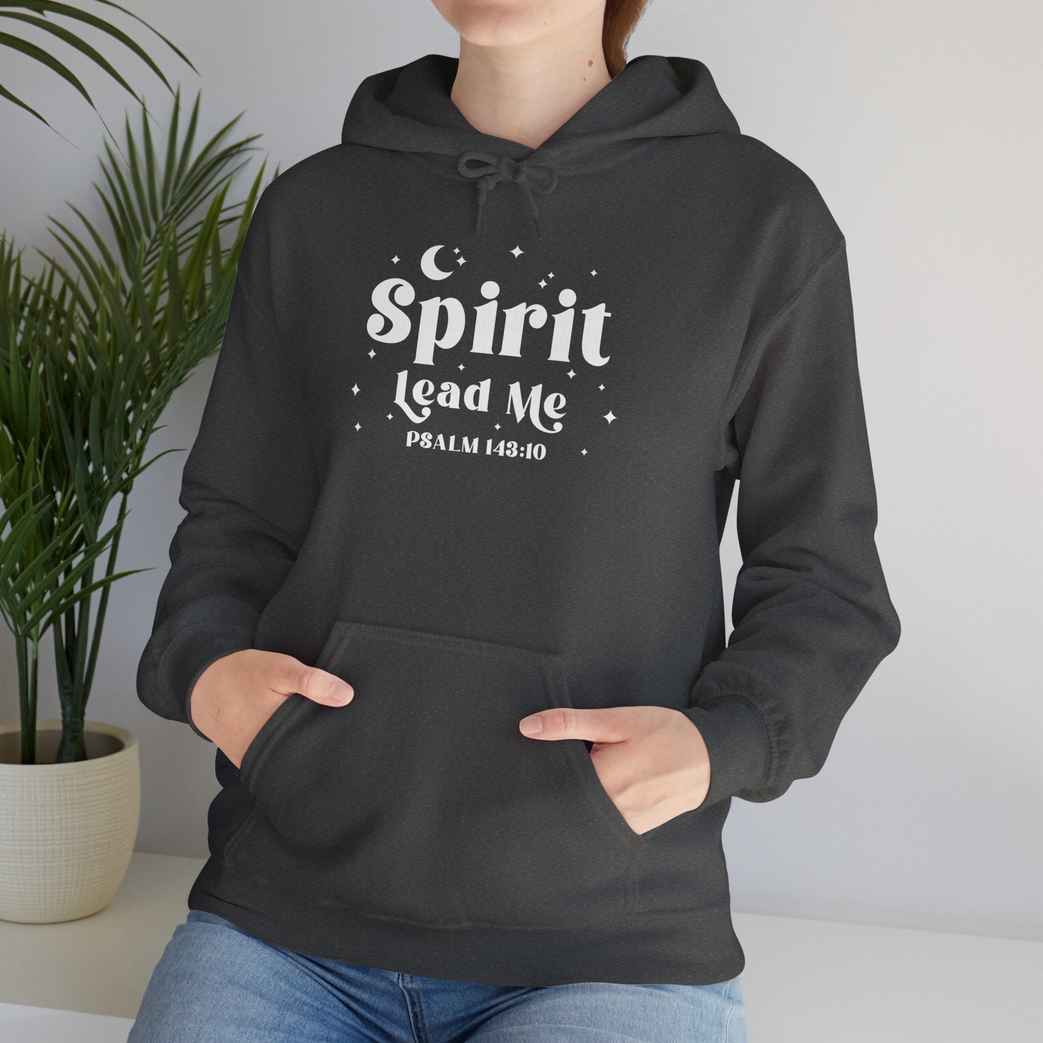 Person wearing a dark heather gray hoodie with 'Spirit Lead Me' text, standing indoors with a plant in the background.