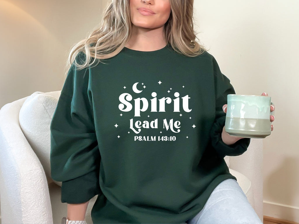 Person wearing a forest green sweatshirt with 'Spirit Lead Me' text, holding a coffee mug.