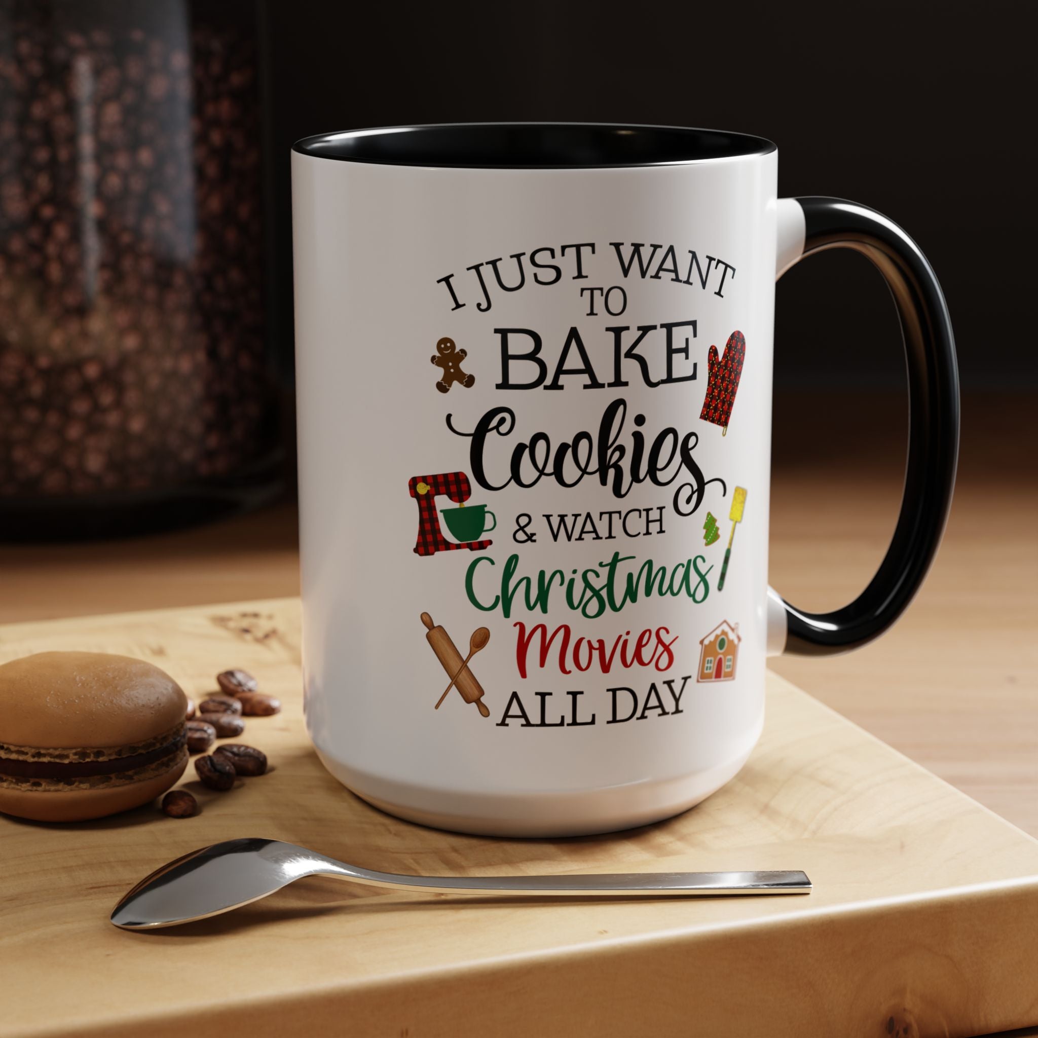 White mug with black interior and handle, featuring text and graphics on a wooden surface with cookies and a spoon.
